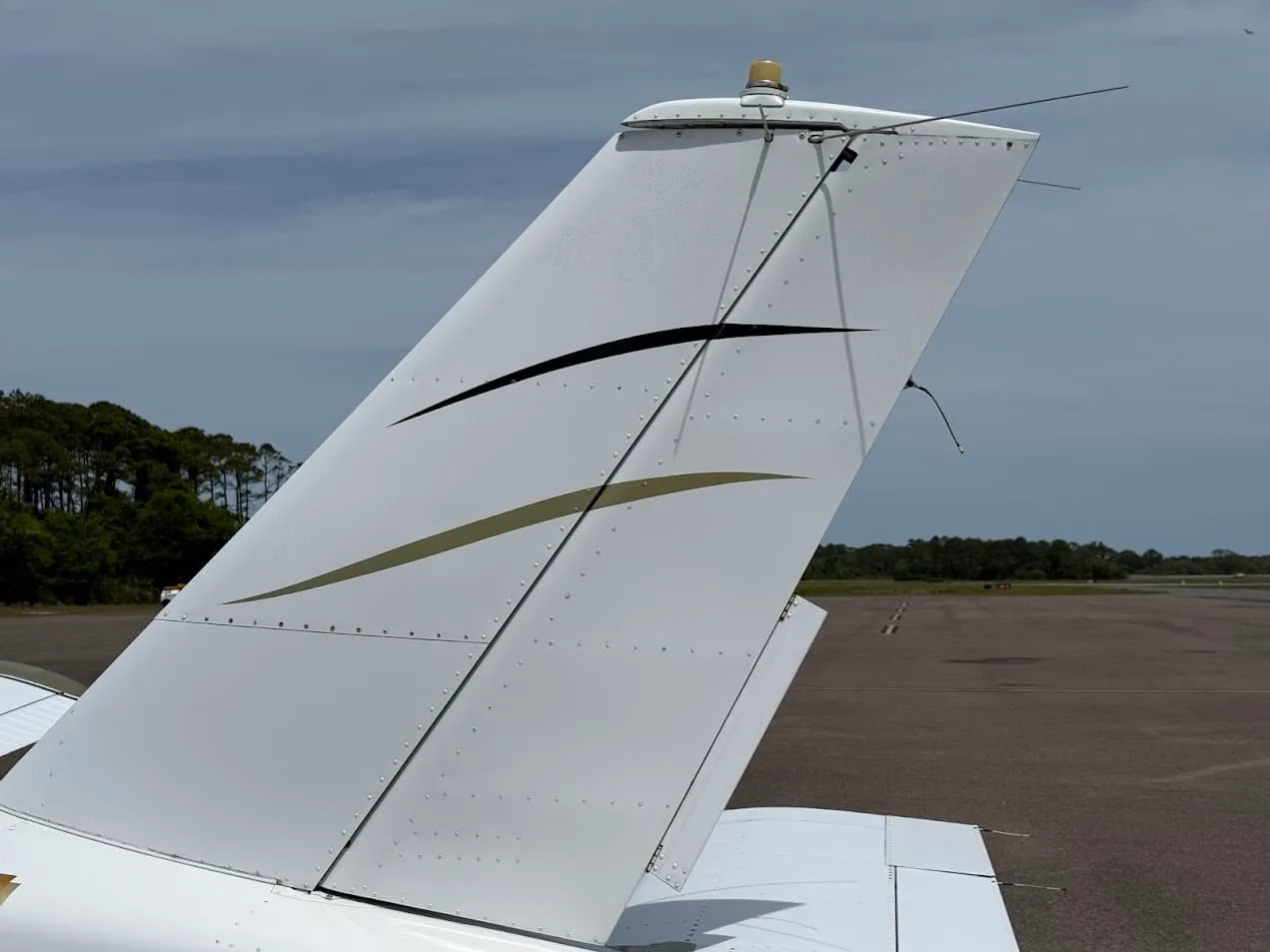 A close-up view of the white vertical stabilizer and rudder with gold and black stripes on the Socata TB-20 Trinidad aircraft.