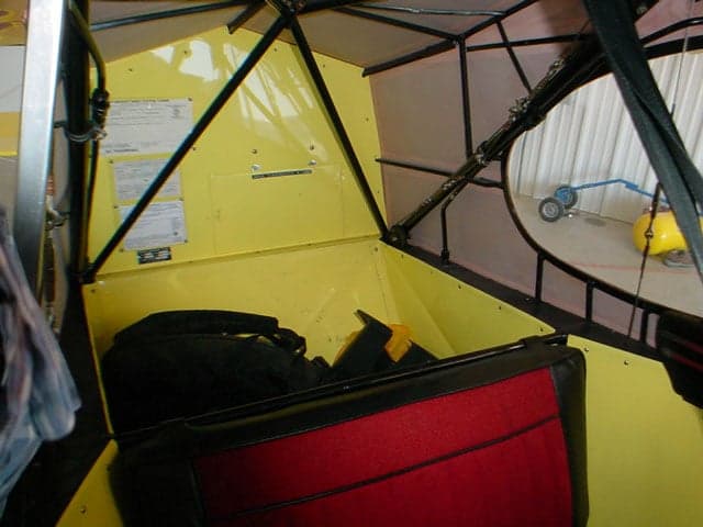 The rear interior cabin of the Piper Super Cub aircraft, showing red seats and yellow walls.