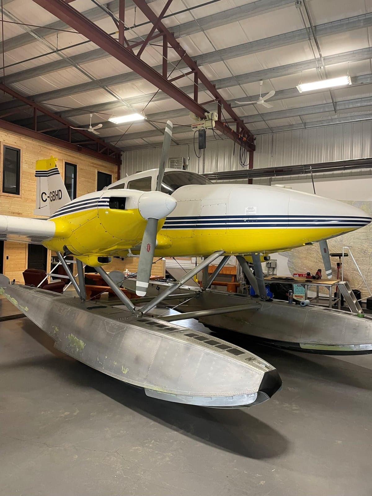 Yellow and white twin engine aircraft on floats, parked outside a hangar.