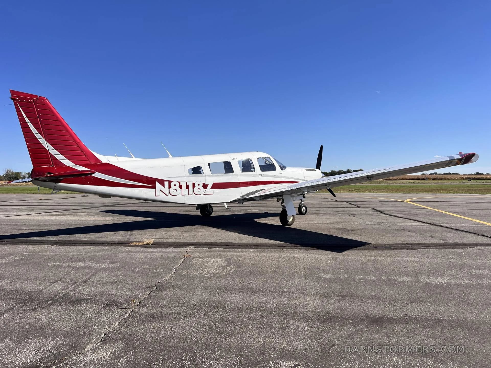 A white single-engine propeller aircraft with red and white tail and stripes, registration N8118Z, parked on an asphalt ramp under a clear blue sky.