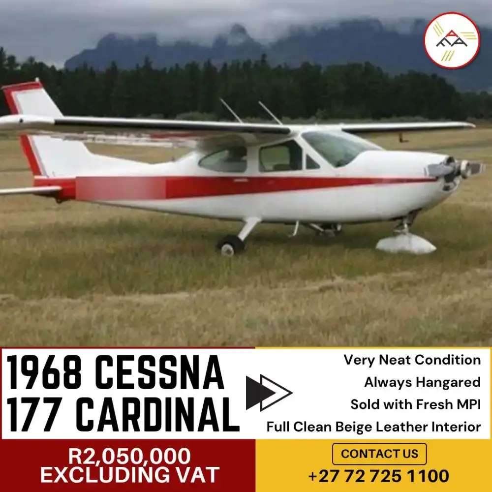 A white Cessna 177 Cardinal with red stripes is parked on a grassy field, with mountains in the background.