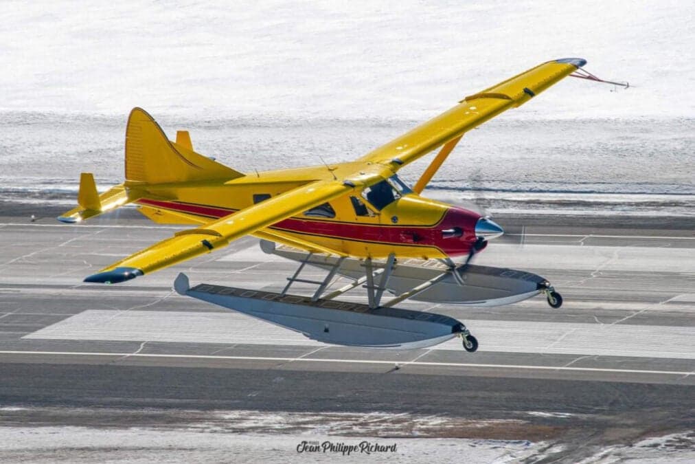 Yellow and red floatplane taking off from a snowy runway.