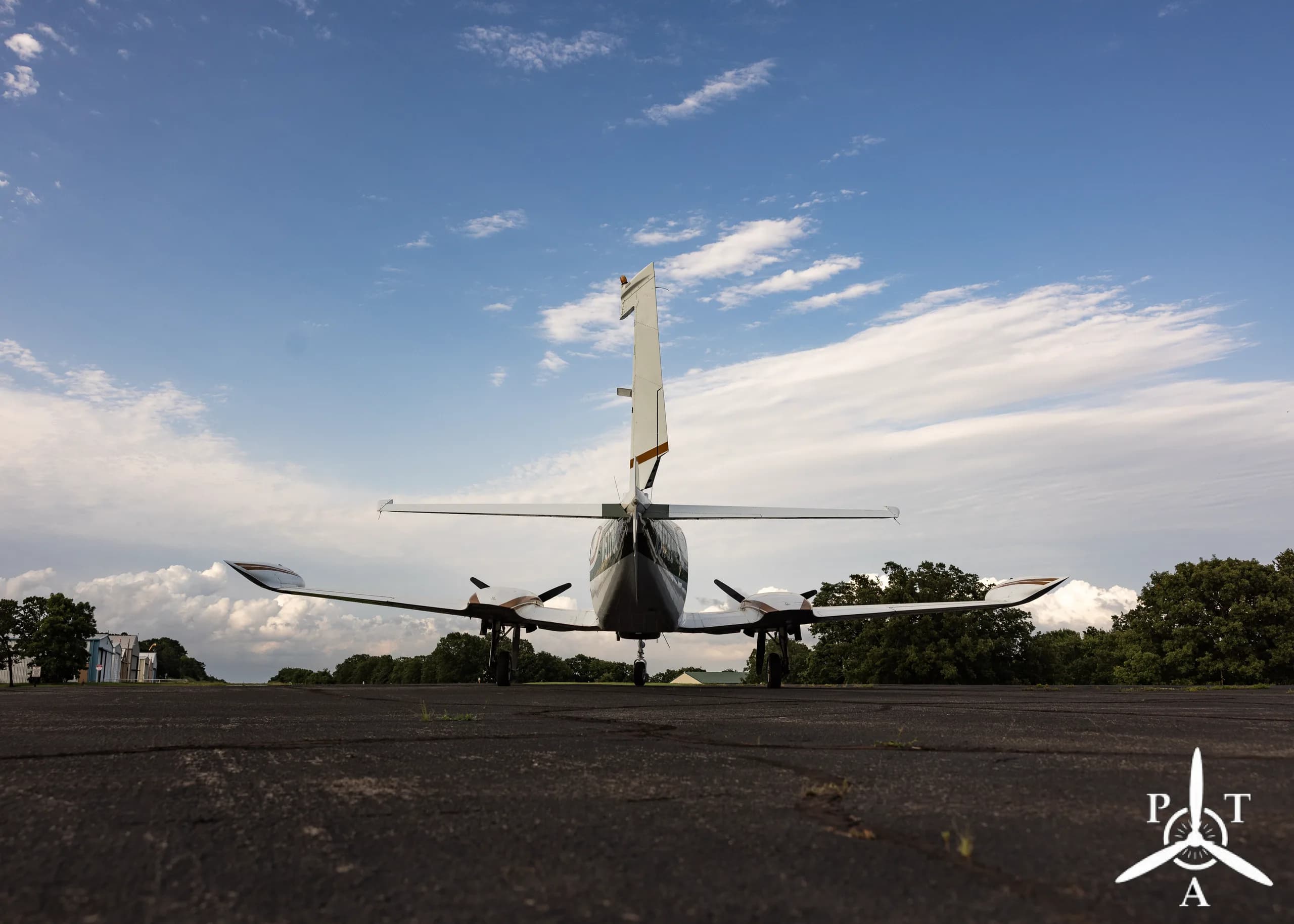 A rear view of a white and green Cessna 340A twin-engine aircraft, N5178J, parked on an asphalt ramp under a blue sky.