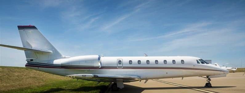 A white jet aircraft is parked on the tarmac under a blue sky.