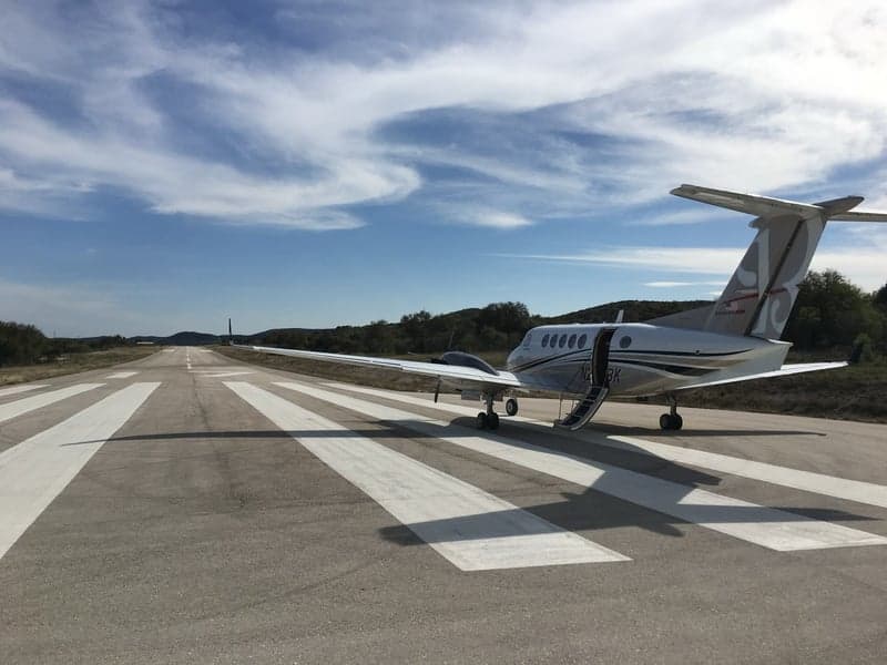 A King Air aircraft with tail number N205BK is parked on the runway with the door open.
