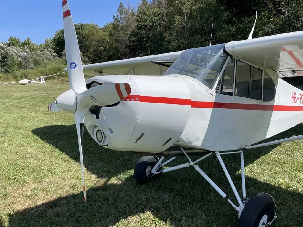 A close-up view of the front of a white single-engine aircraft with a red-striped propeller and nose cone.