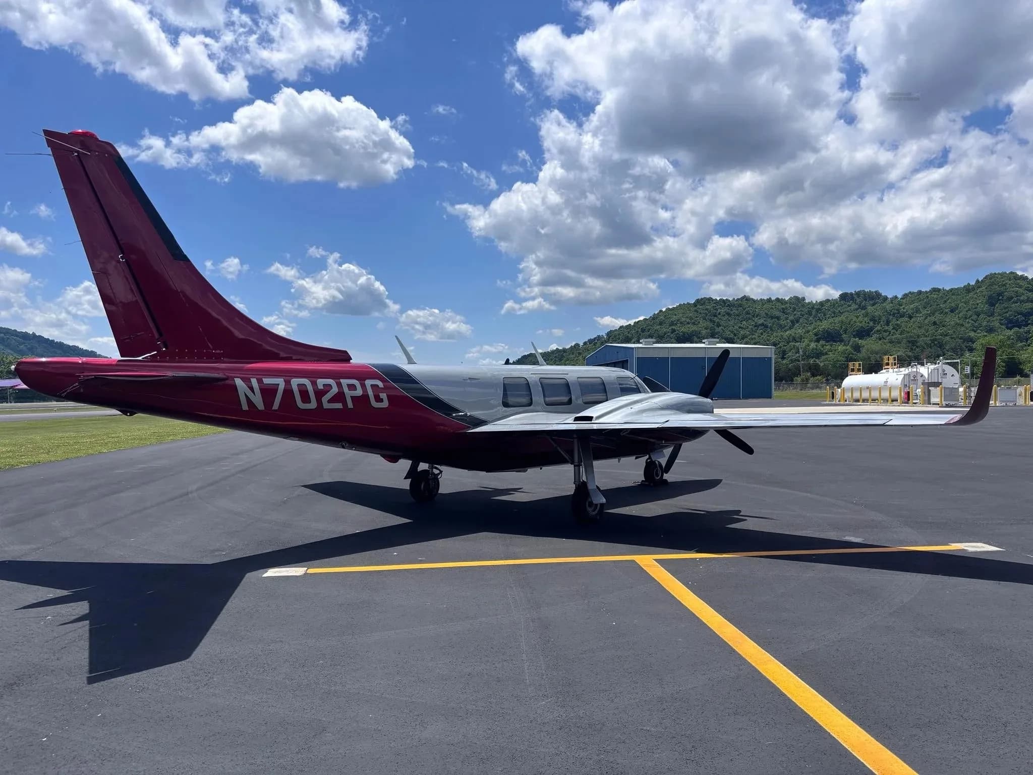 A rear three-quarter view of a silver and red twin-engine Aerostar aircraft (N702PG) on an airfield.