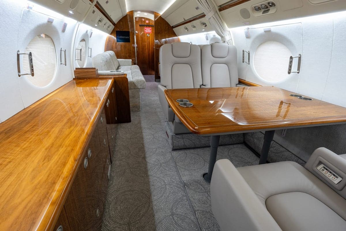 The aircraft's interior features a table, seating, and wood trim.