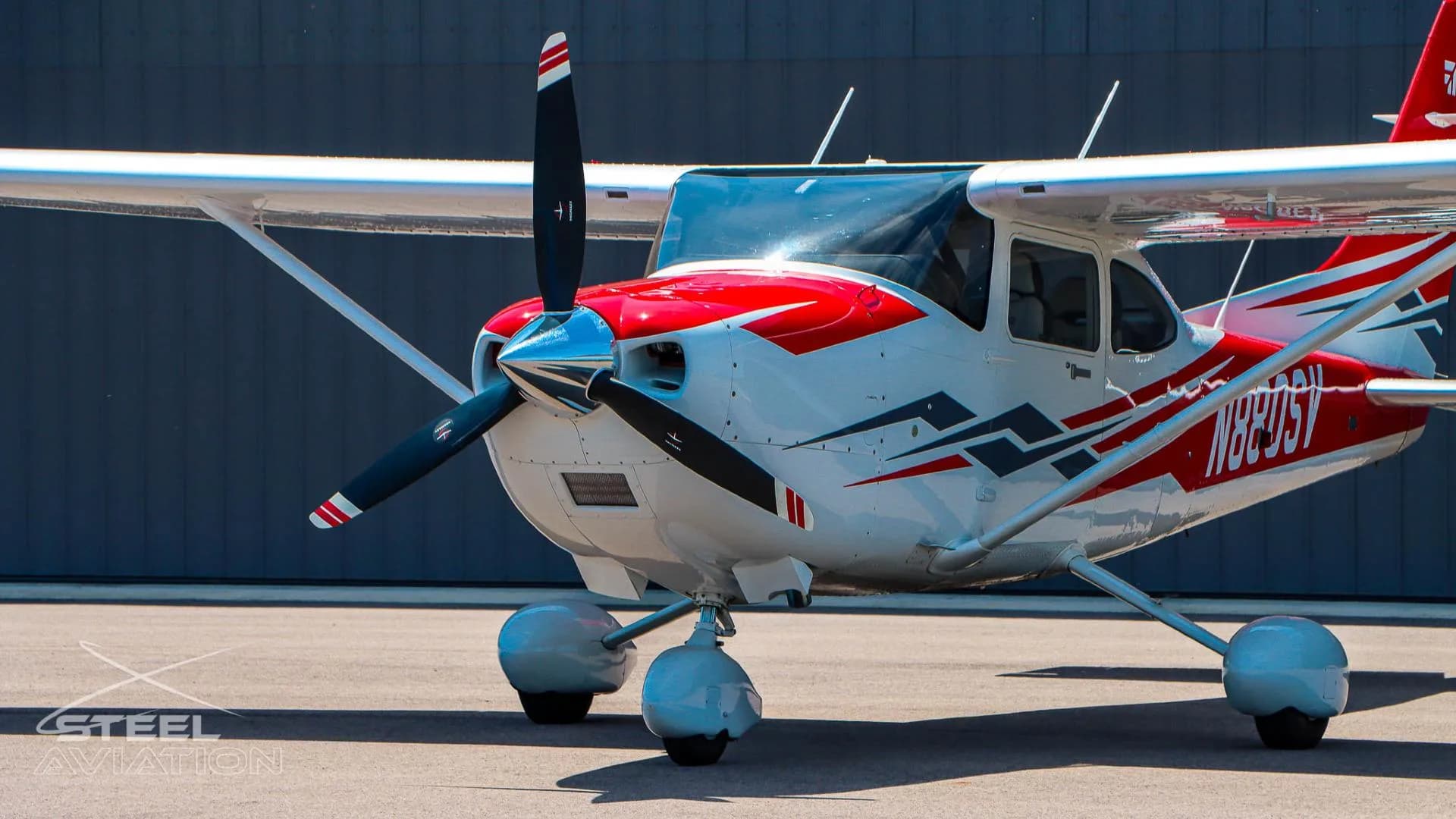 A close-up of the front fuselage and propeller of a white Cessna T182T Skylane TC with red and grey stripe details.