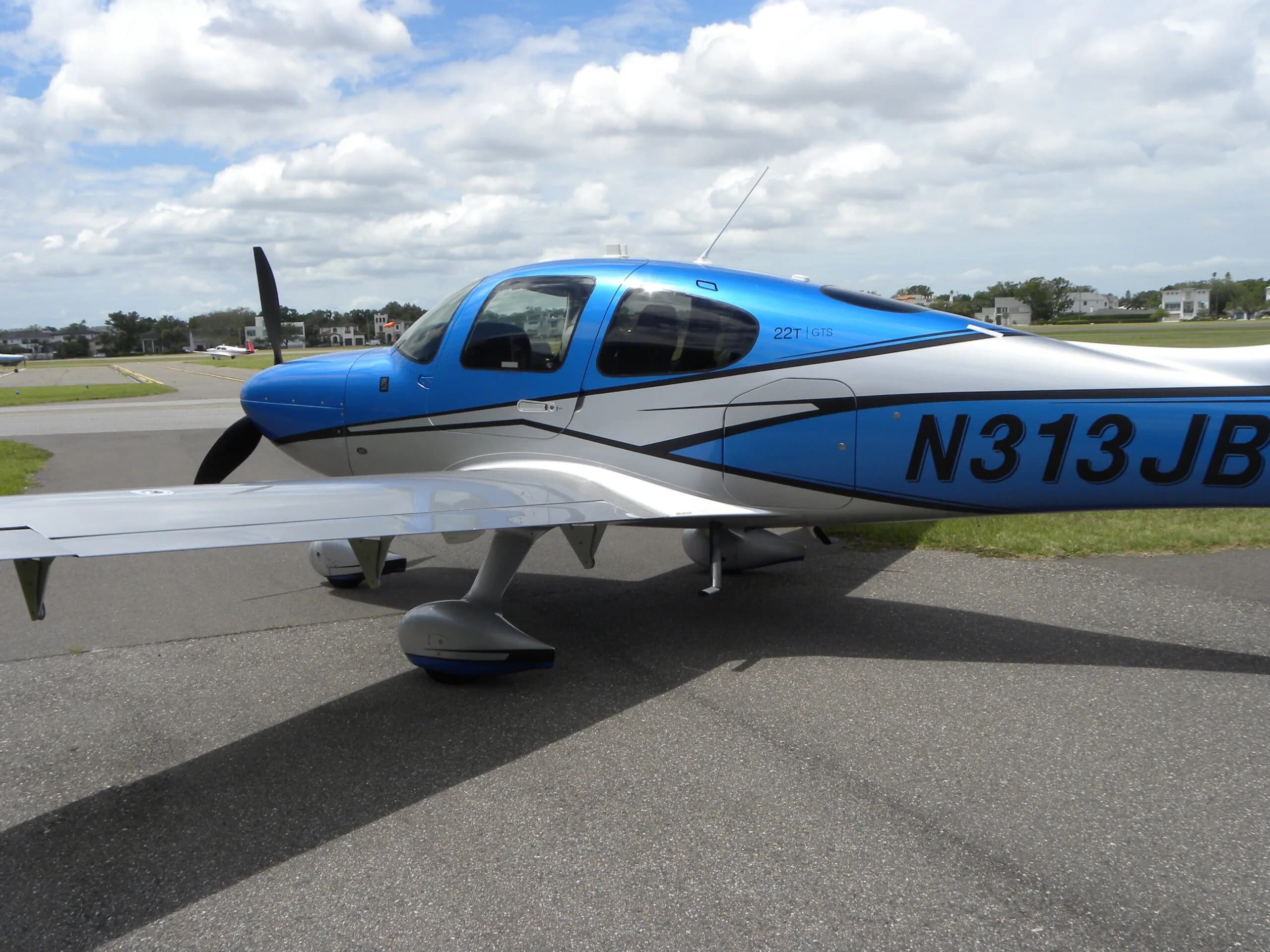 A blue and silver Cirrus SR22T aircraft, N313JB, on an airport tarmac under a cloudy sky.