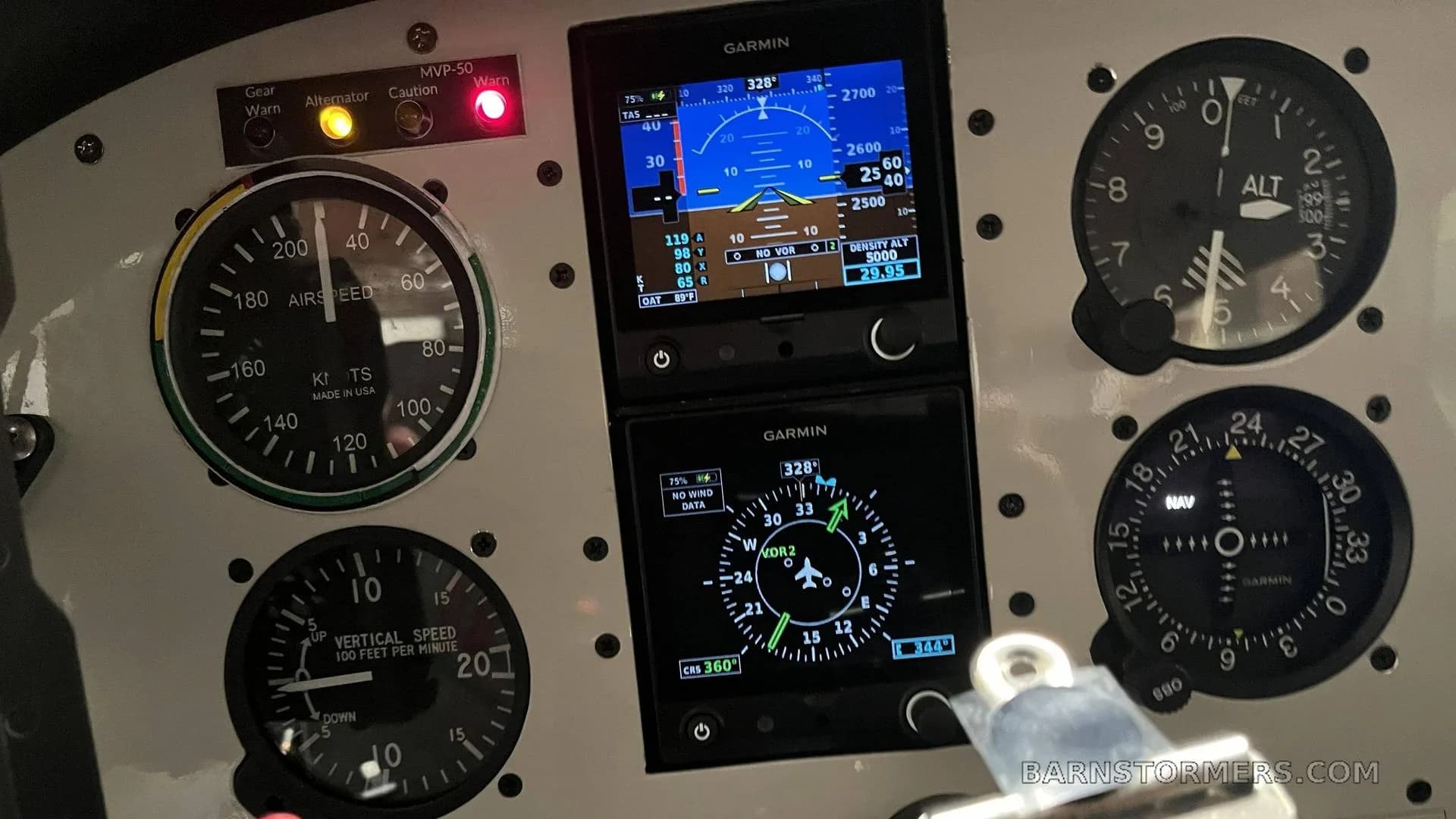 A close-up of the aircraft instrument panel, featuring analog gauges and two Garmin digital displays showing flight information.