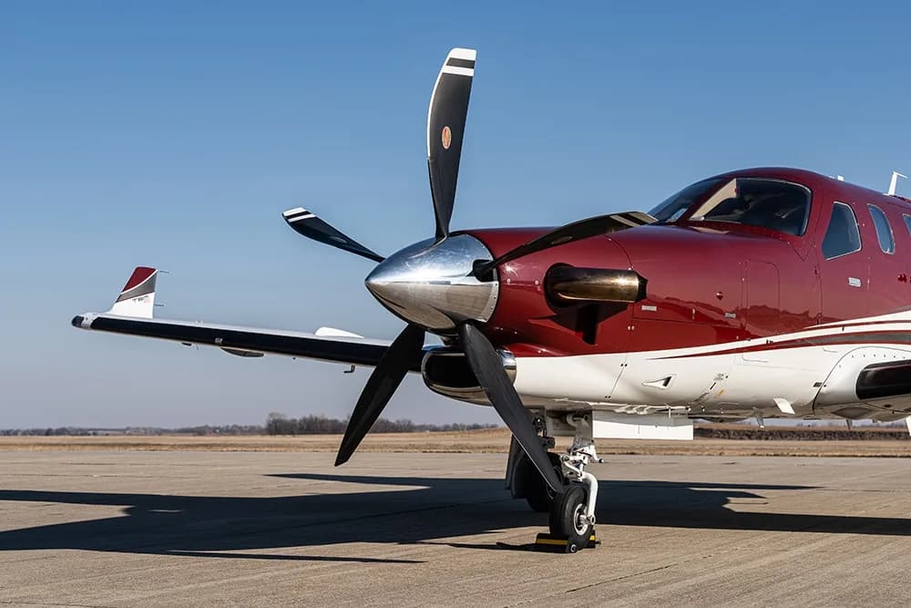 Close-up of the front of a maroon and white Daher TBM 900 aircraft, highlighting the propeller and engine cowling.