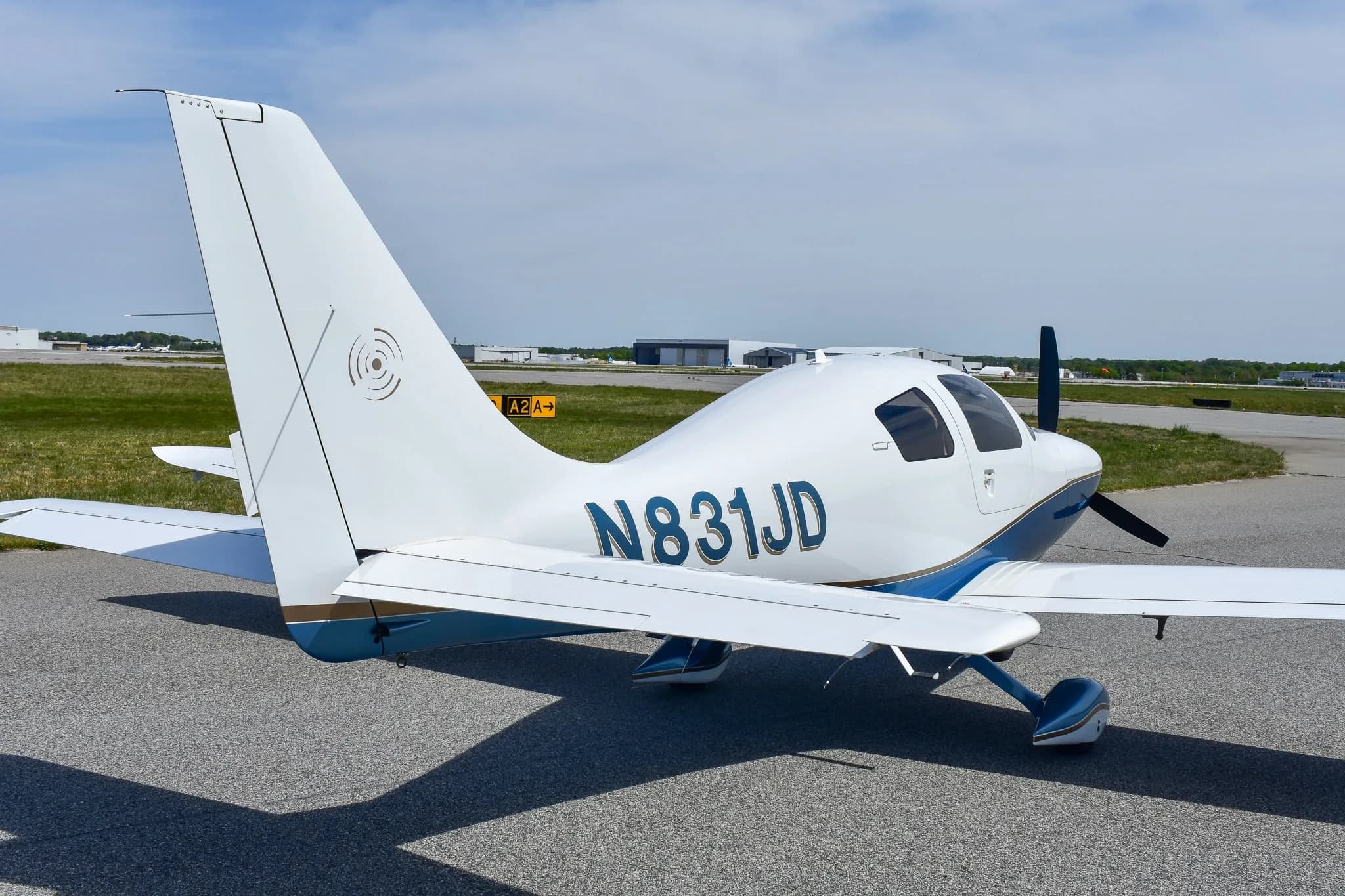 Rear three-quarter view of a white and blue single-engine aircraft with registration N831JD on an airfield.