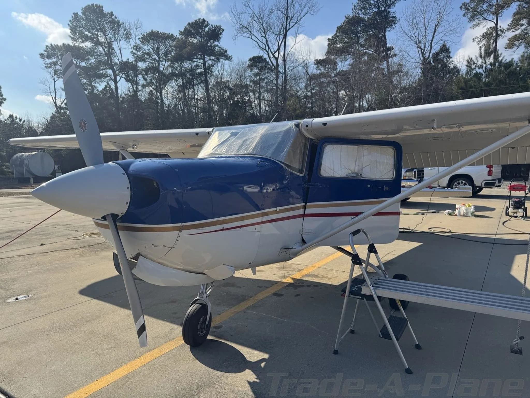 A front-left view of the blue and white Cessna 182 Skylane N9326D with a ladder next to its wing.