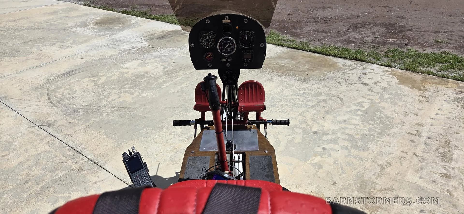 A view from the pilot's seat of an ultralight aircraft, showing the instrument panel and a handheld radio.