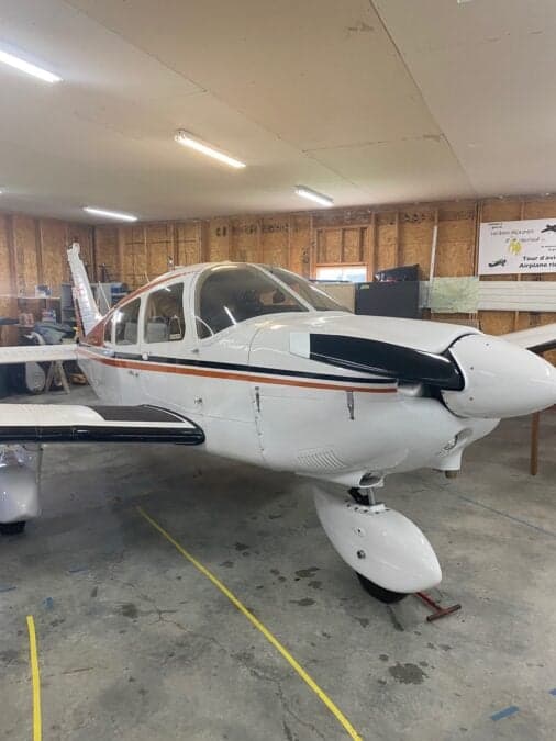 Front view of a white and orange aircraft with a black propeller in a hangar.