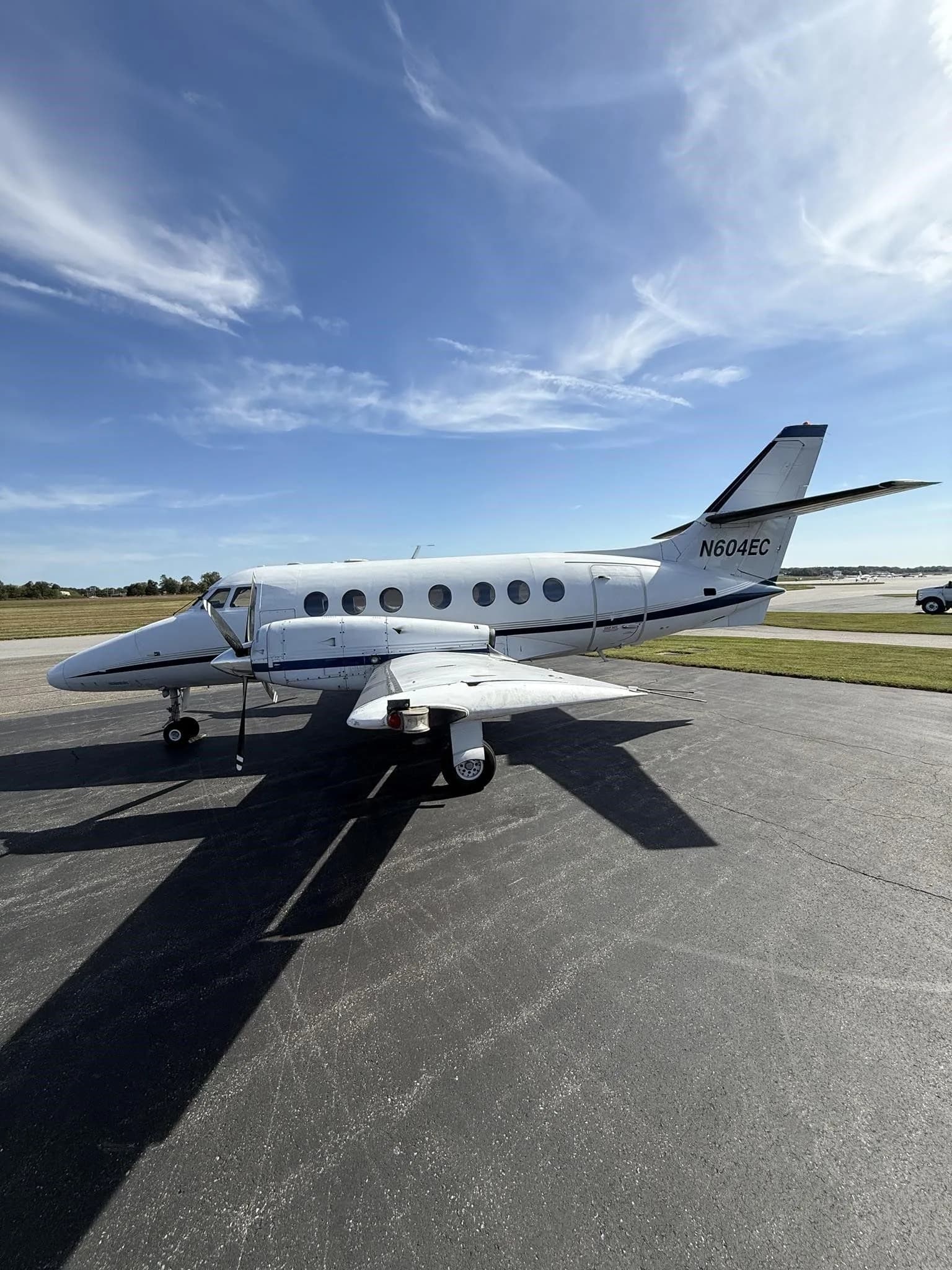A white Jetstream 31 aircraft with blue accents, tail number N604EC, parked on an asphalt tarmac under a blue sky.