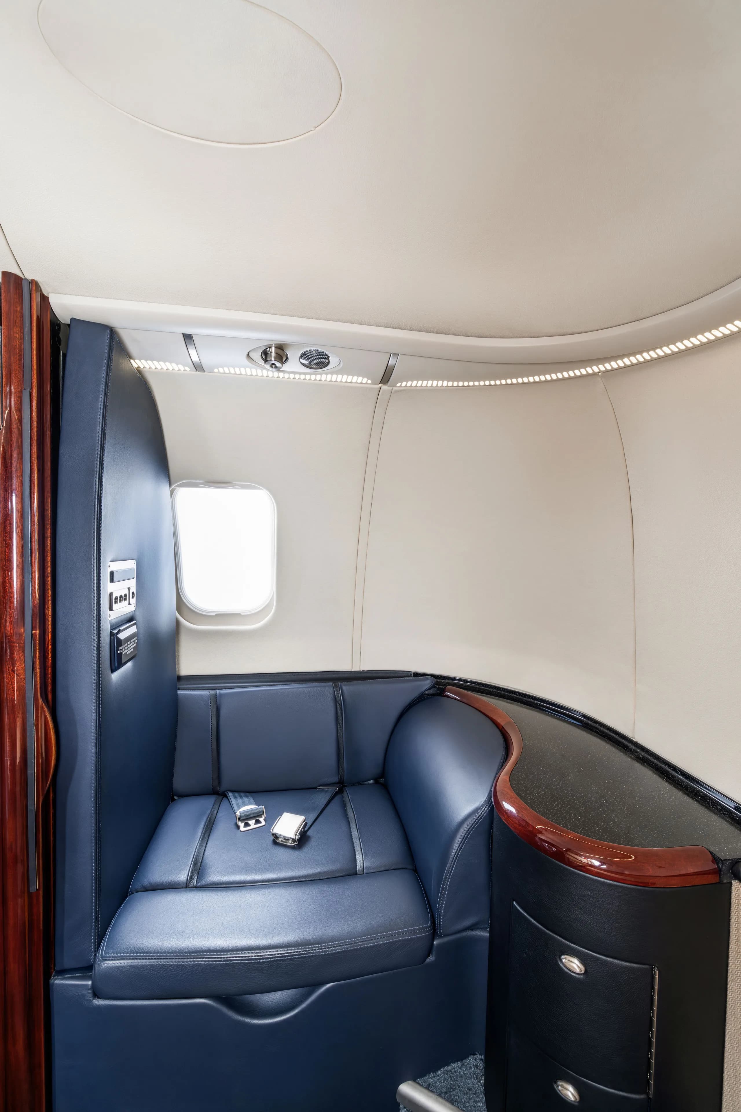 A side view of a private jet's interior, showing a dark blue leather couch-style seat next to a window and wood-trimmed cabinetry.