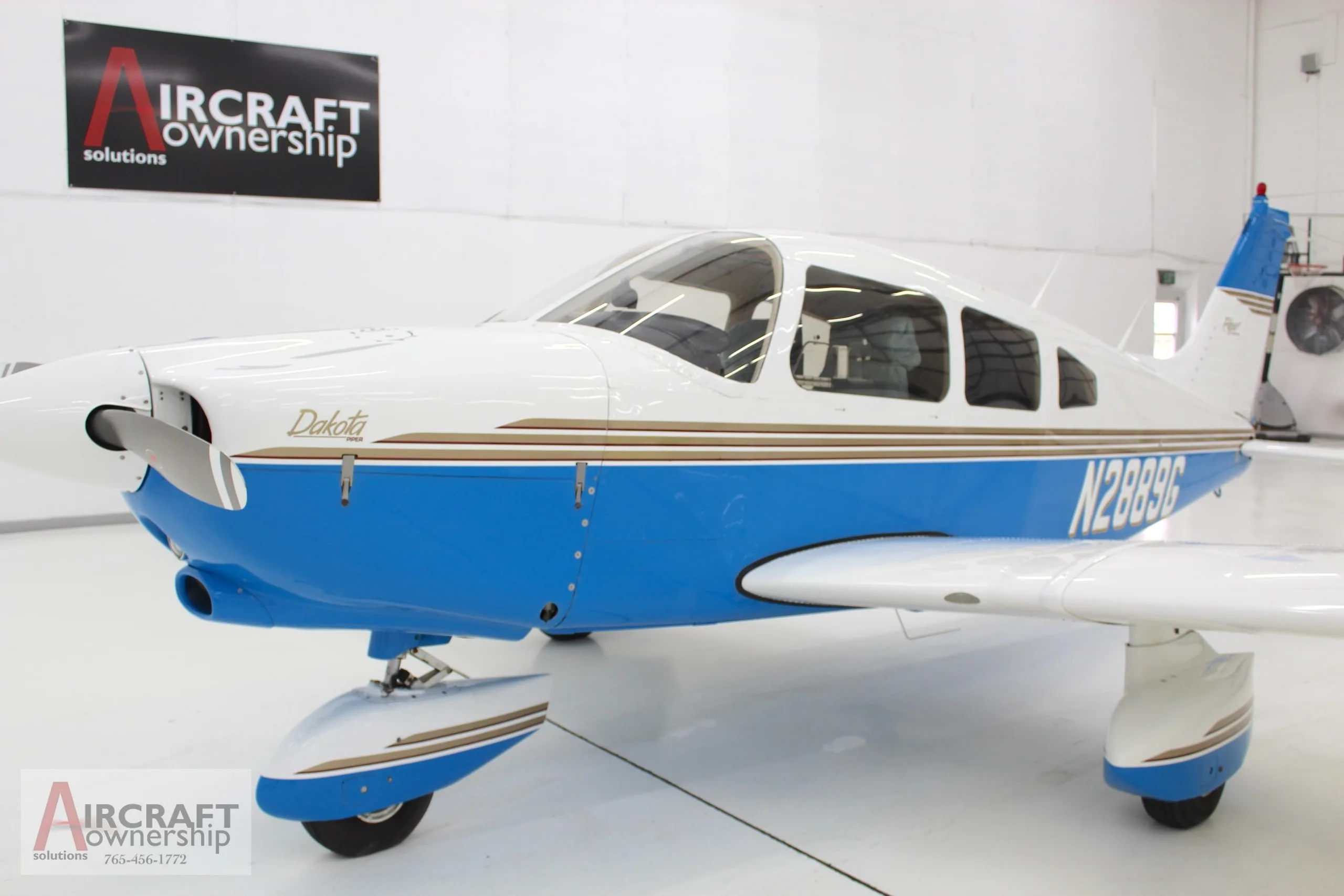 A front-side view of a white and blue Piper Dakota aircraft with N2889G registration, parked in a hangar.