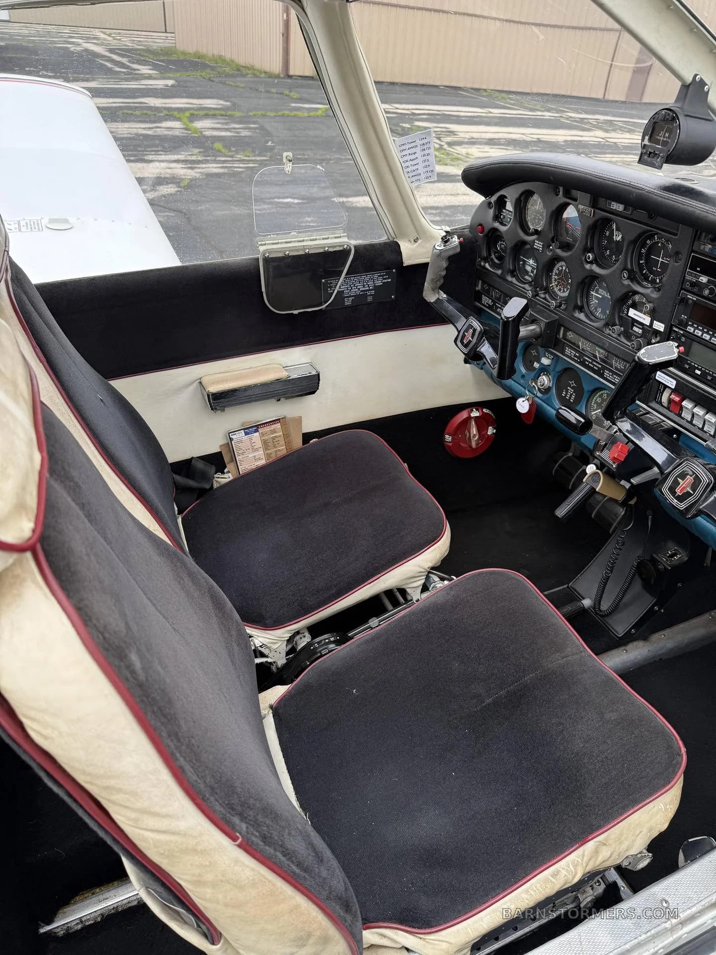 The interior of a light aircraft showing the two front seats with black and beige upholstery and a partial view of the instrument panel.
