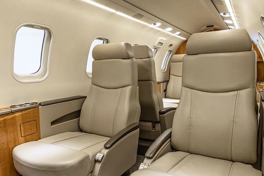 A close-up view of the beige leather seats and a window inside a private jet cabin.