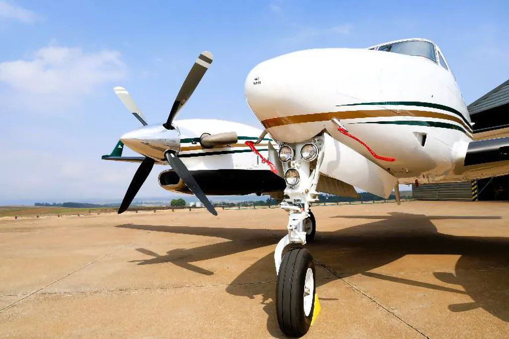 A close-up view of the front landing gear and right engine of a white Beechcraft King Air C90GTx aircraft on a tarmac.