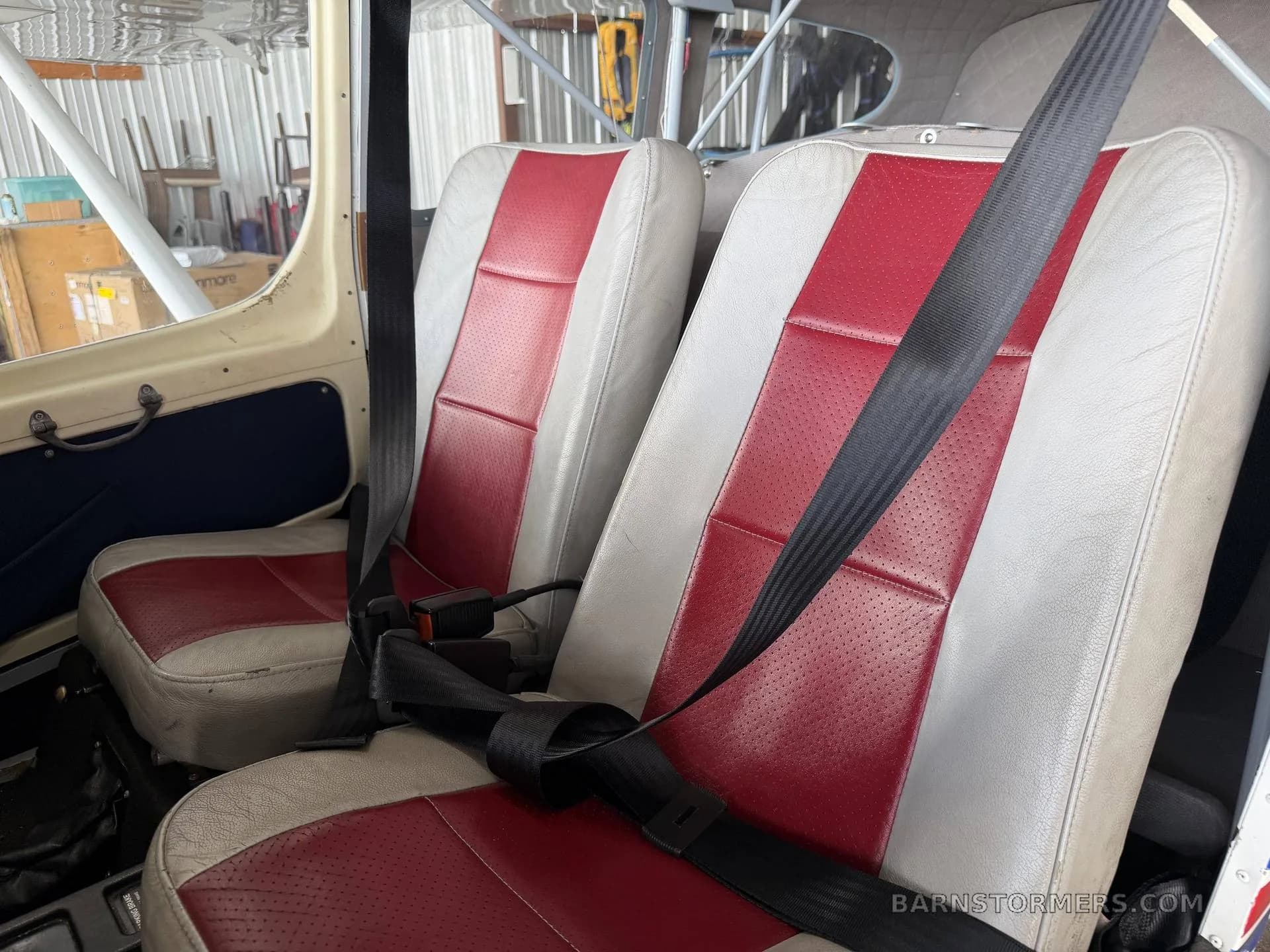 The red and white two-tone seats of a light sport aircraft cabin with seatbelts fastened.
