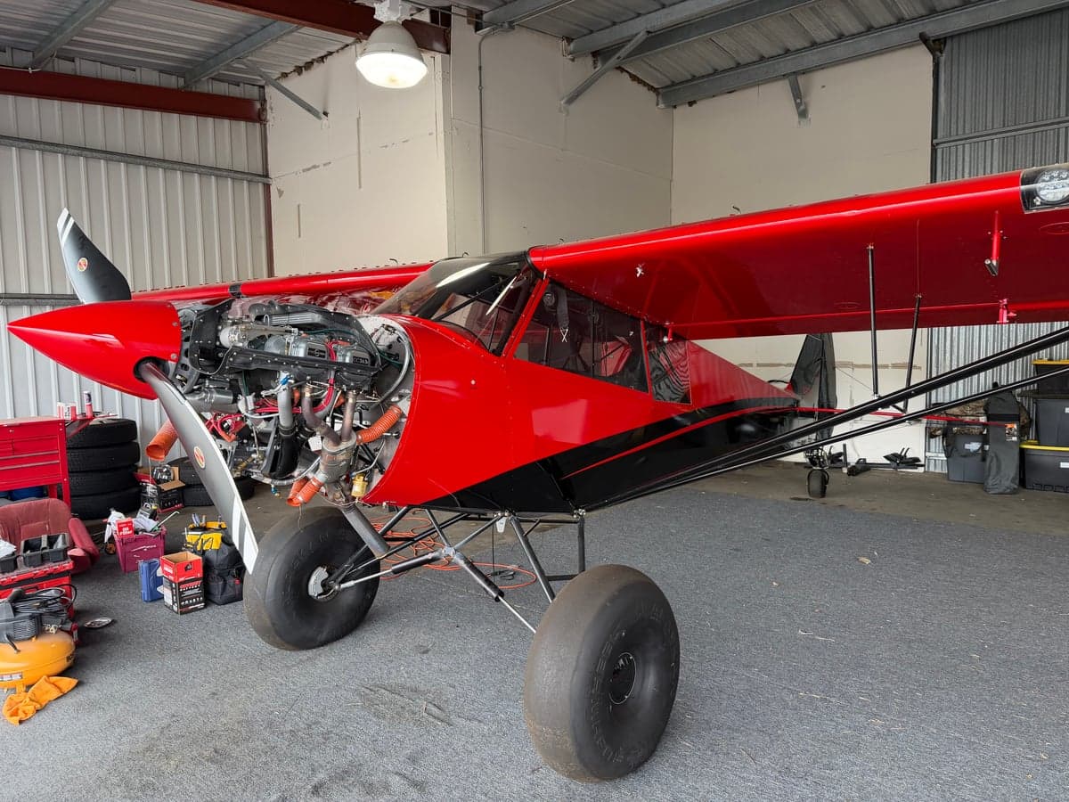 Side view of the red and black N83ZC aircraft with the engine exposed in a hangar.
