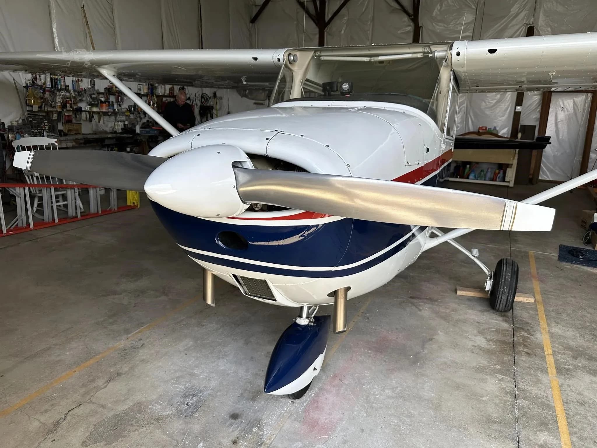 A head-on view of the white and blue Cessna N7959U with a red stripe in a hangar.