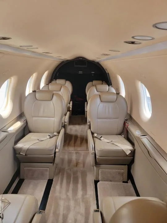 The passenger cabin of a Pilatus PC-12 aircraft, showing rows of tan leather seats and a carpeted aisle.