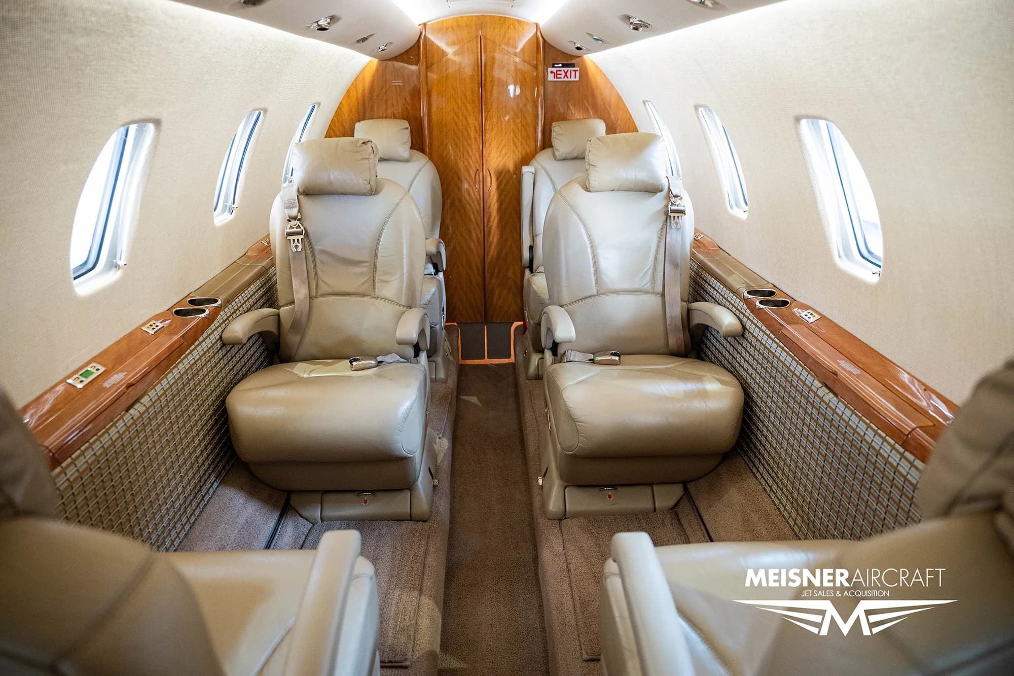 The interior cabin of a business jet with tan leather seats and wood paneling, looking towards the rear, with a 'Meisner Aircraft' logo.