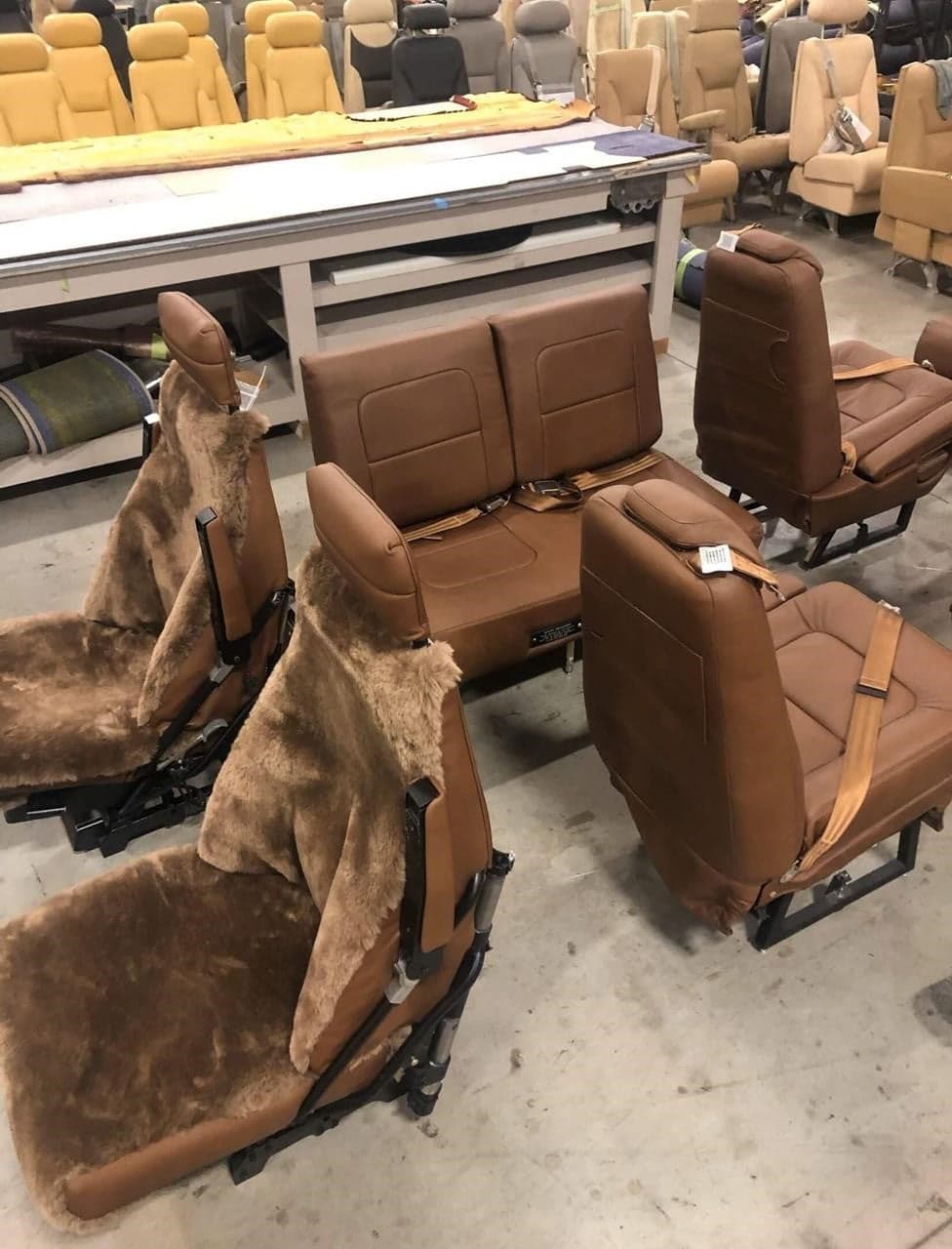 Aircraft seats with brown leather and sheepskin covers in a workshop setting.