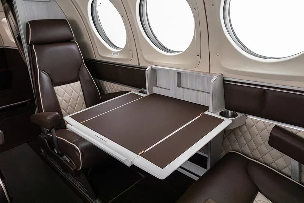 A brown and beige quilted aircraft seat next to a deployed fold-out table with a brown surface.
