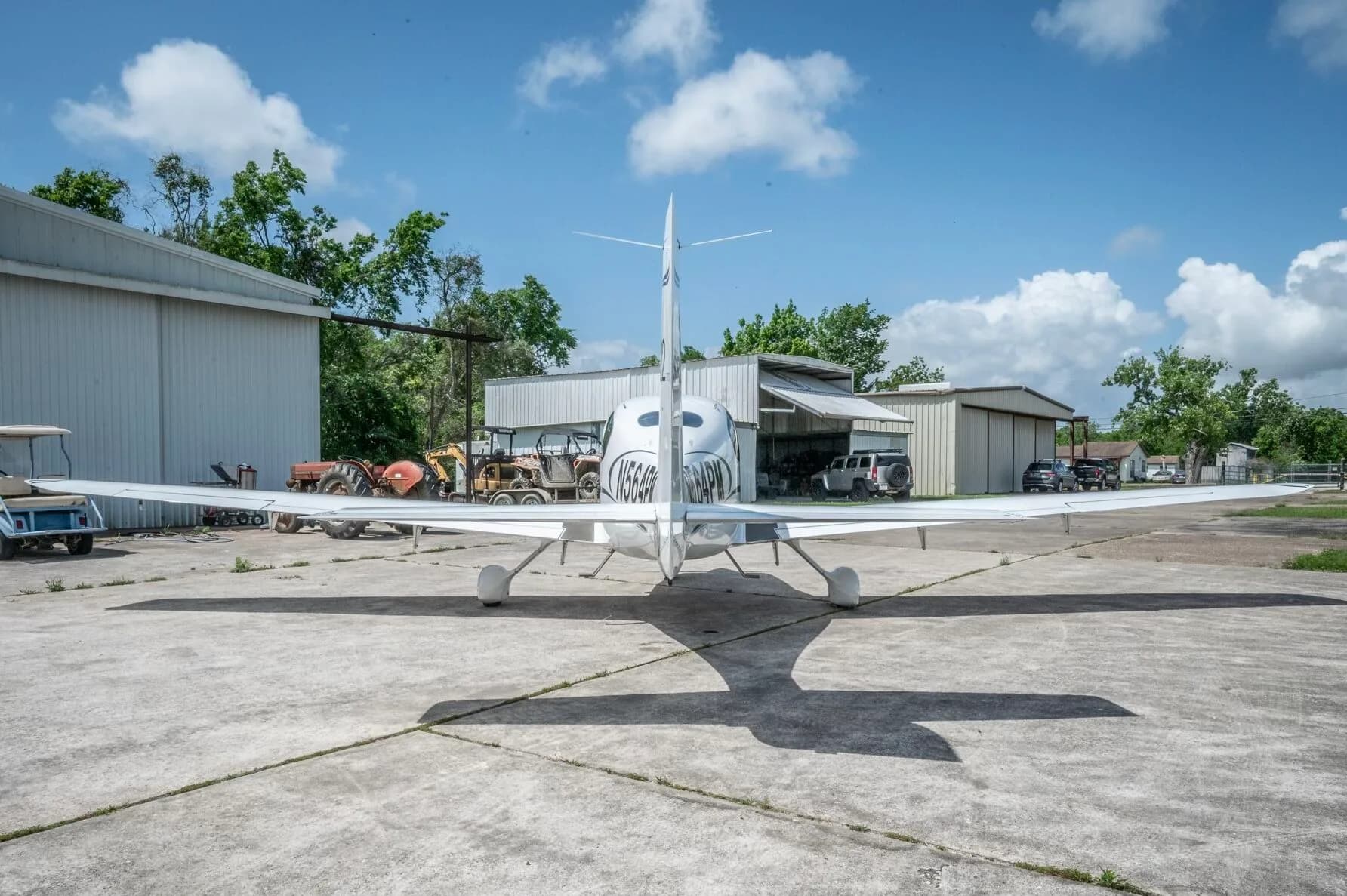 A rear view of a white Cirrus SR22 GTS aircraft with N564PM registration on the tail, parked on a concrete ramp.