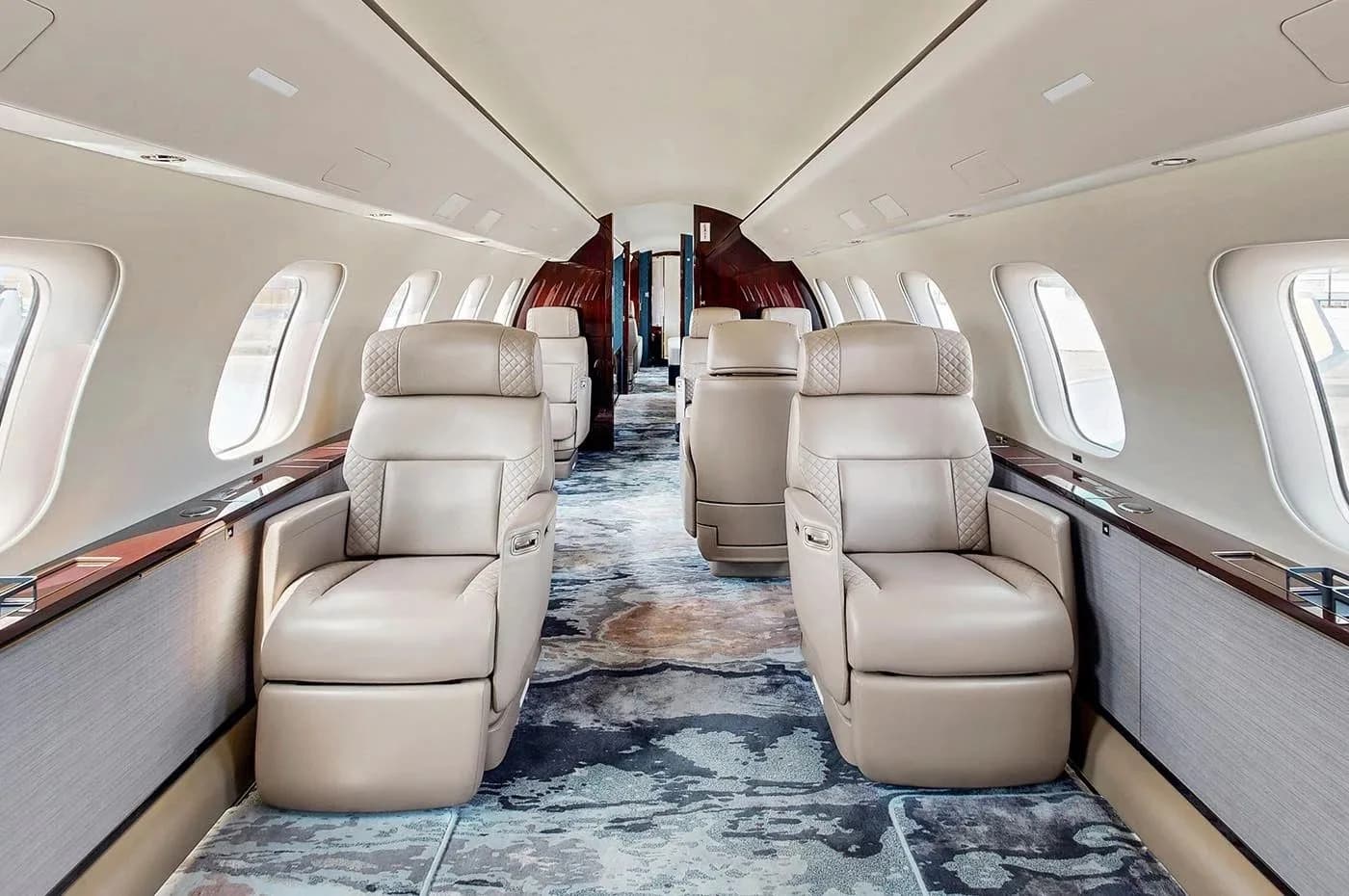 A luxurious private jet cabin with rows of light beige quilted leather seats and a patterned blue and grey carpet.