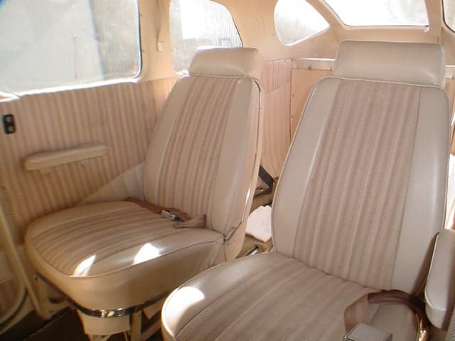 The beige interior cabin of a Cessna 206 aircraft, showing two front passenger seats with striped fabric inserts.