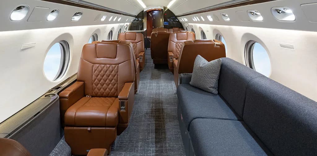 The luxurious cabin interior of a business jet, featuring brown leather seats and a grey sofa.
