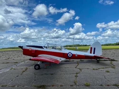 Side view of a red and white aircraft with British markings on a cracked concrete runway.