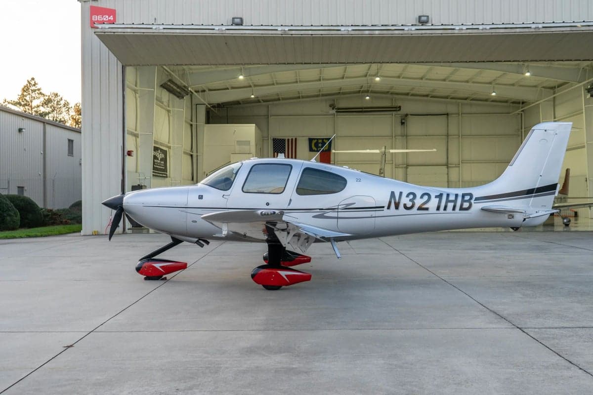 A Cirrus SR22T aircraft with a silver paint scheme parked outside a hangar.