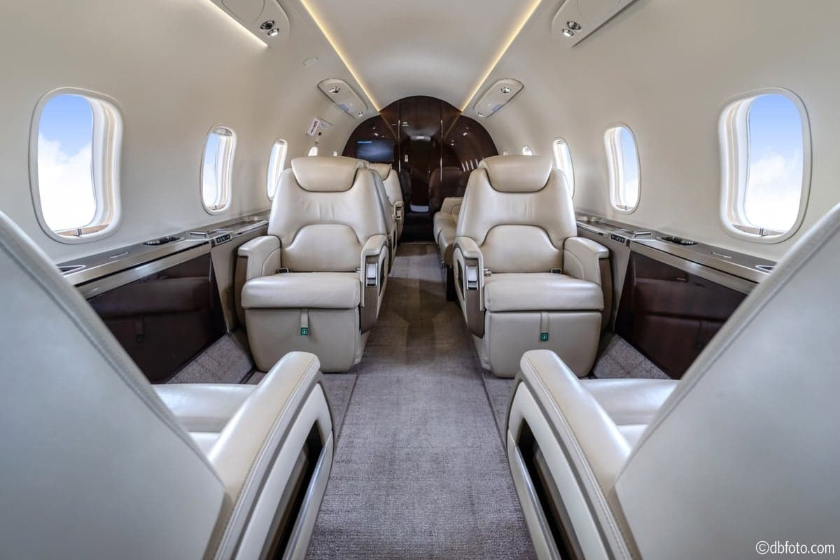 The spacious main cabin of a business jet with cream leather seats and dark wood accents.