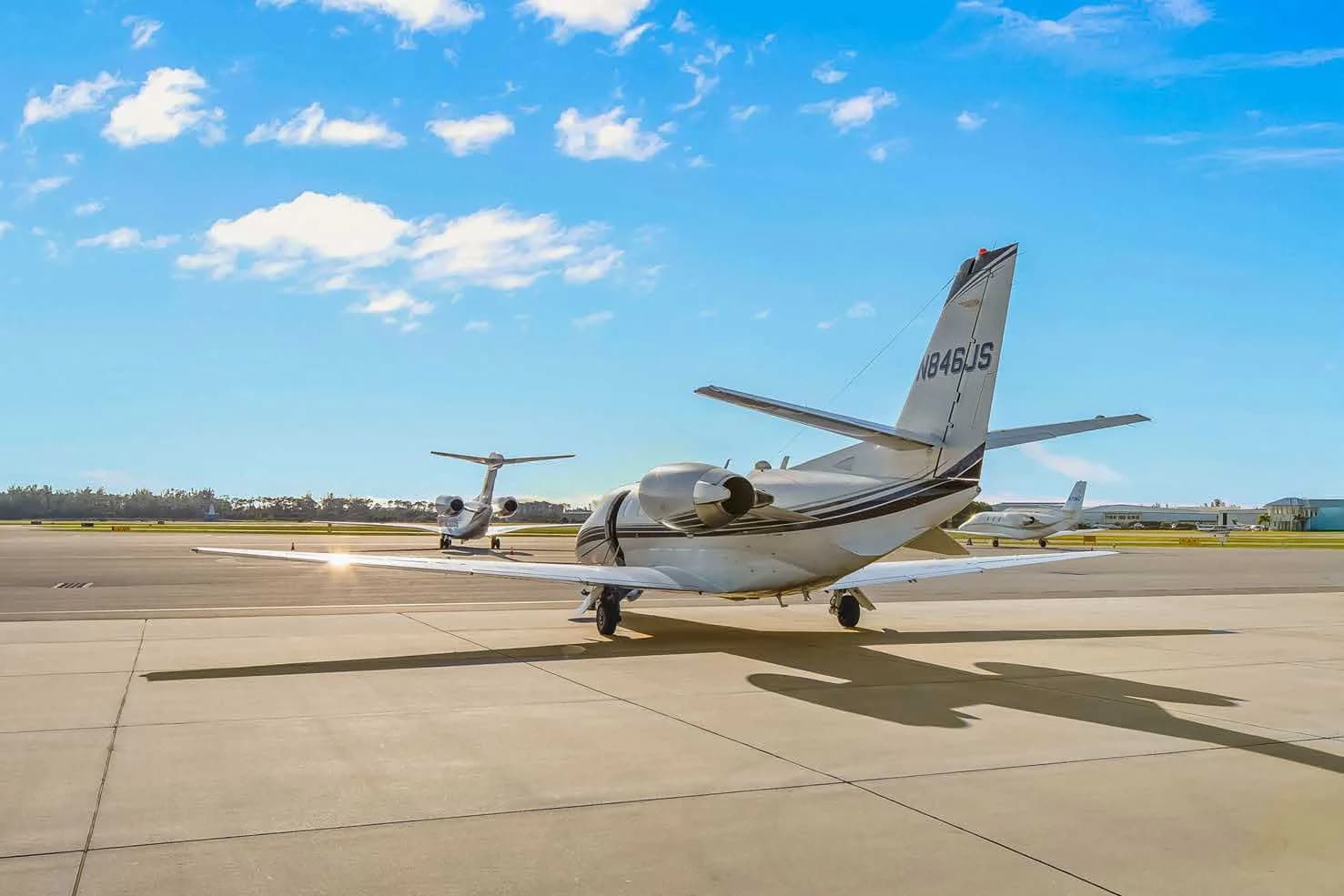 A rear three-quarter view of a white Cessna Citation business jet, N846JS, parked on an airport tarmac with other aircraft in the distance.