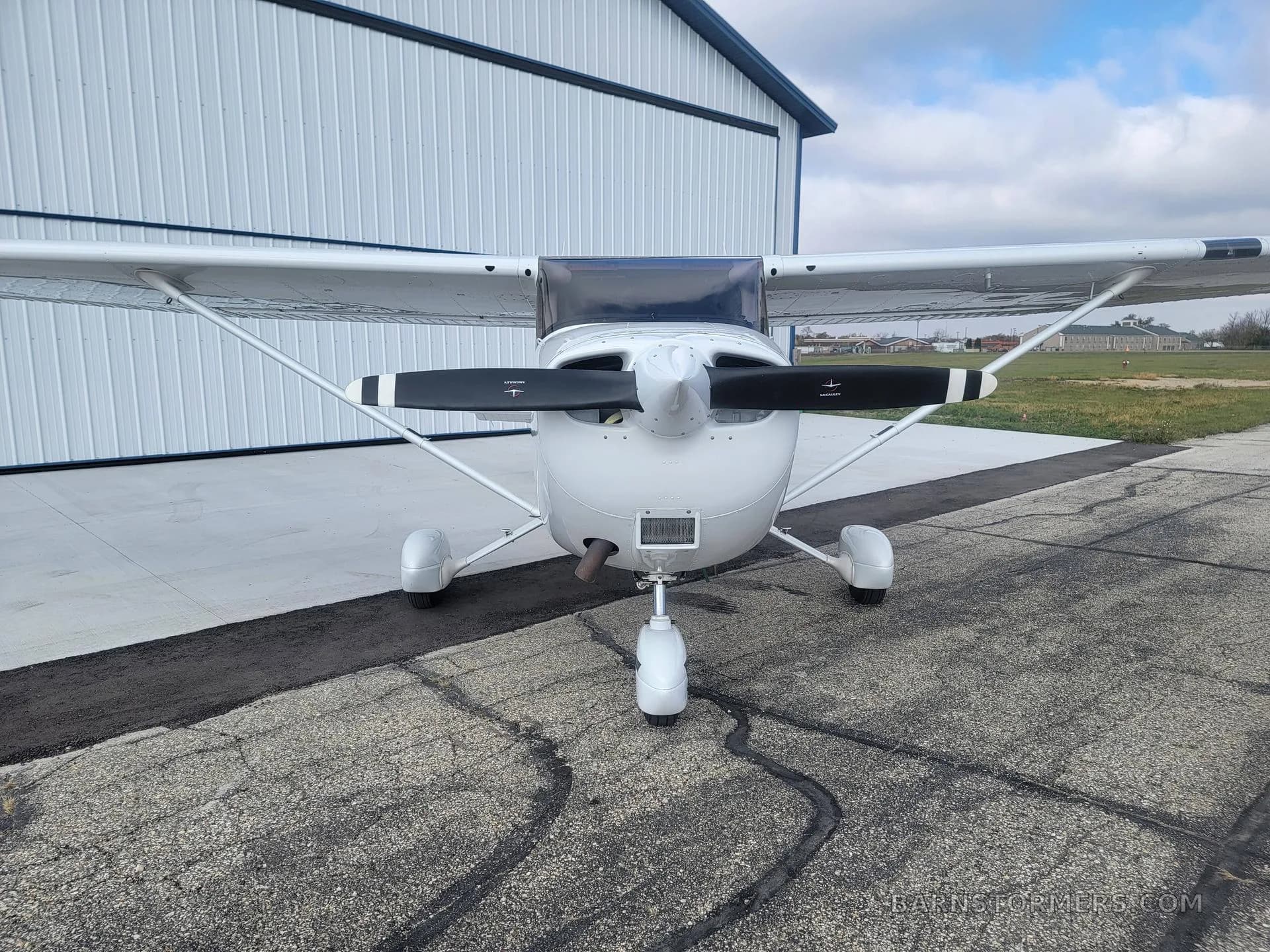 A white Cessna Skyhawk N169CB is shown from the front, parked on an apron in front of a white hangar.