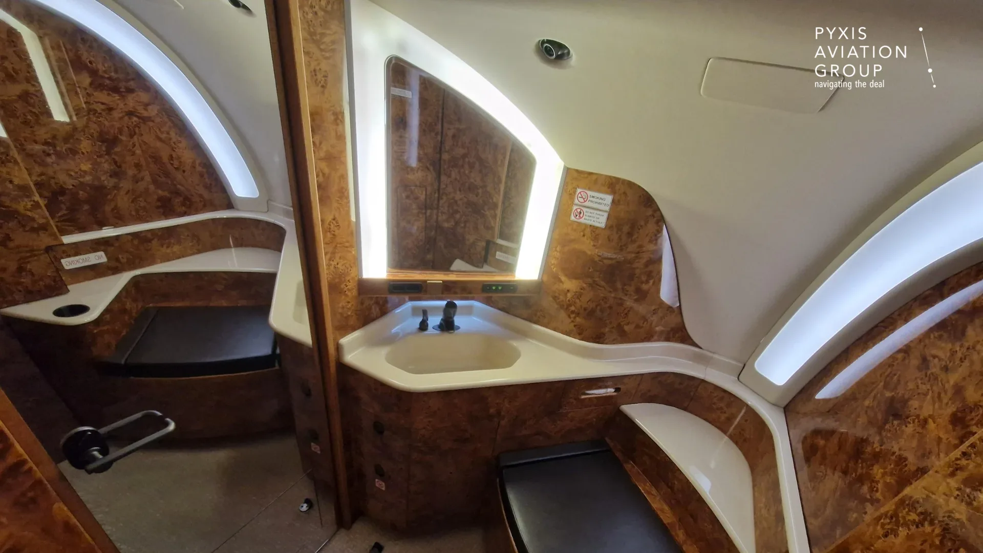 The aircraft lavatory featuring a sink, mirror, and wood-paneled walls.