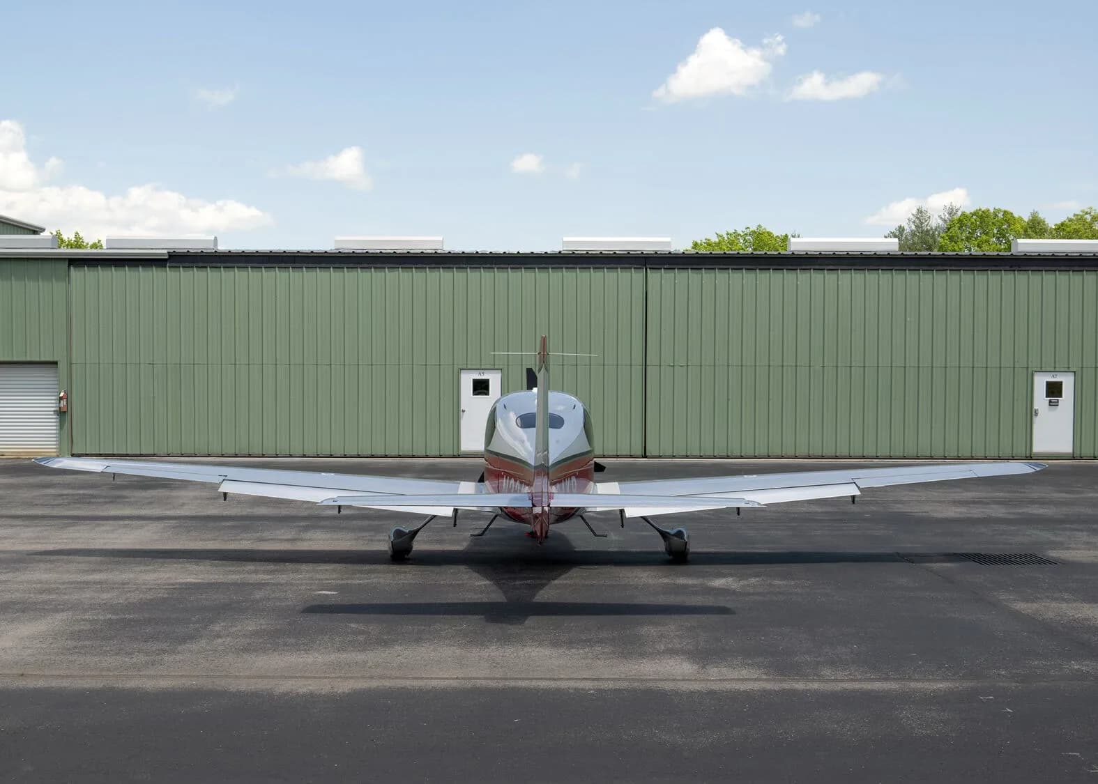 A rear view of a silver and red Cirrus SR22 aircraft, N224KR, parked on an asphalt ramp in front of a green hangar.