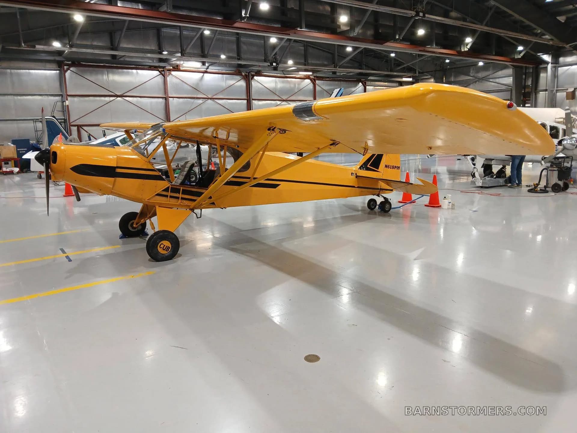 A yellow high-wing aircraft with black accents, seen from the front-left in a hangar.