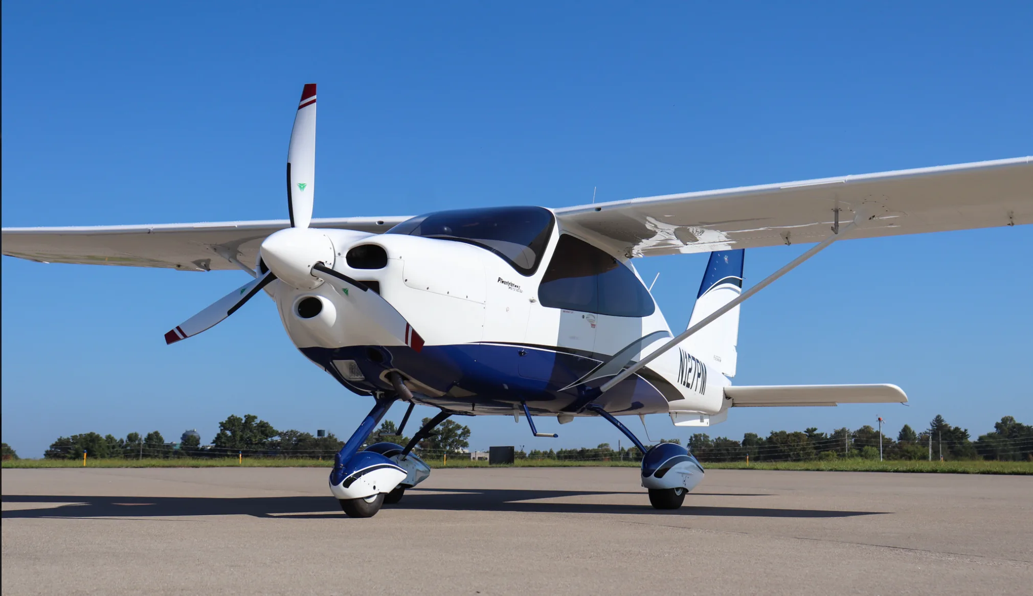 A front-quarter view of the white and blue Tecnam P2010 aircraft, registration N127PM, on an airfield.