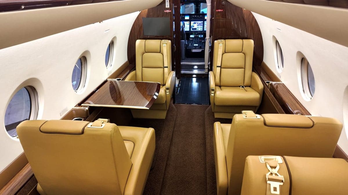 Interior view of the aircraft cabin with tan leather seats facing forward.