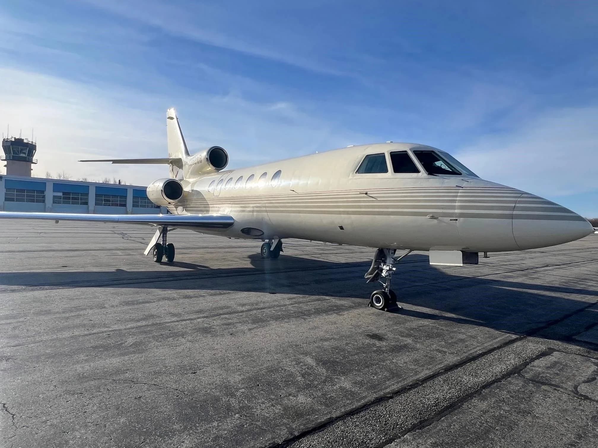 A beige Dassault Falcon 900EX business jet with N352WB registration on the tail, parked on an airport tarmac with a control tower in the background.