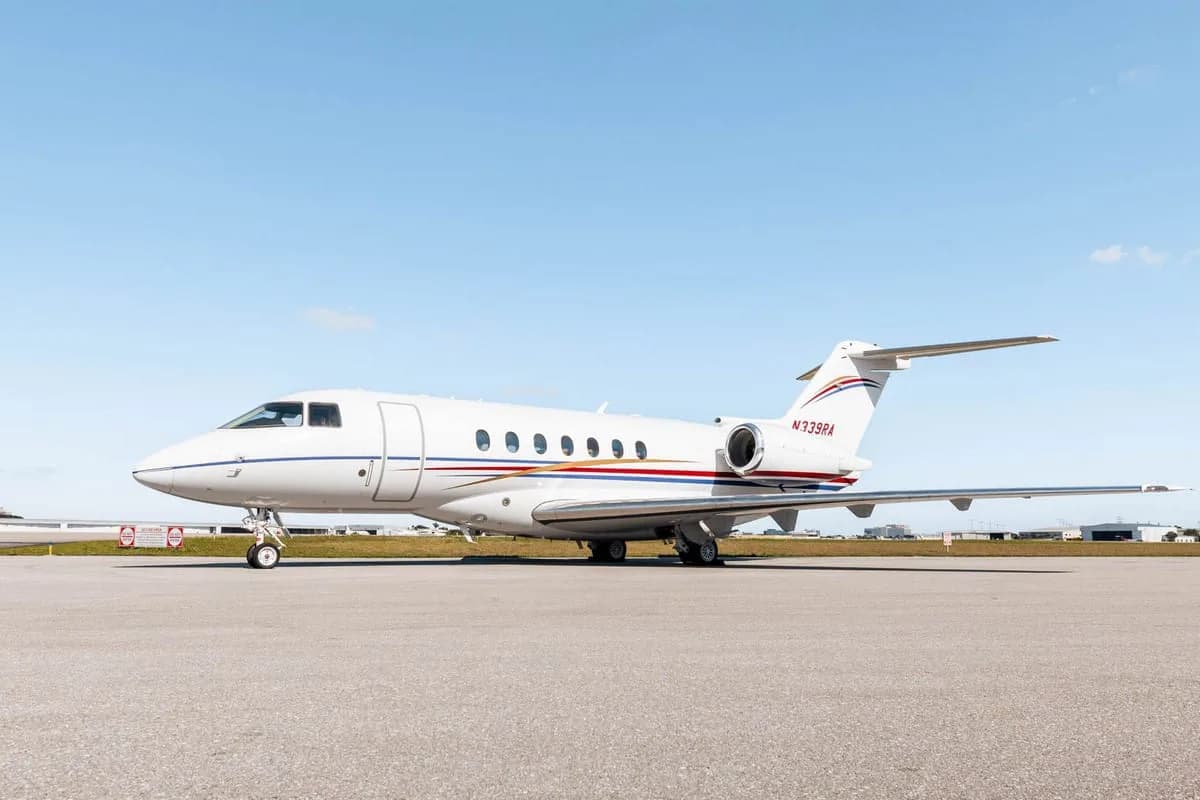 A white Hawker 800XP business jet with red and blue stripes, registration N339RA, parked on the tarmac under a clear sky.