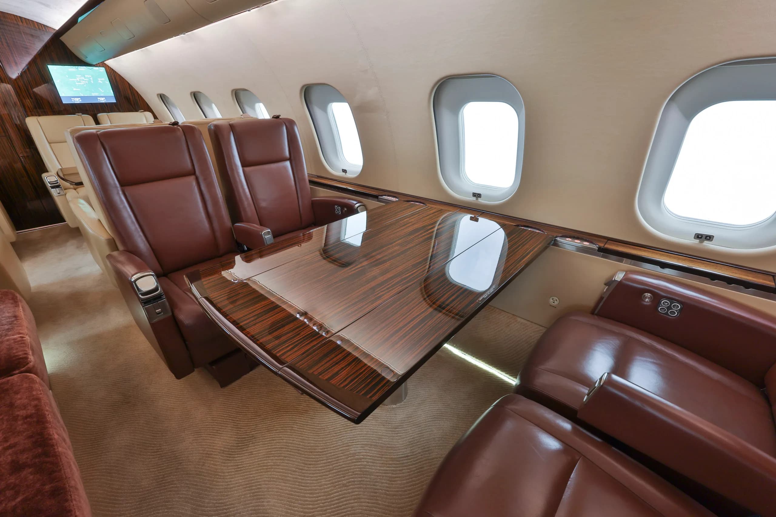 A close-up view of the business jet's cabin, showing brown leather seats, a polished wooden table, and large windows.